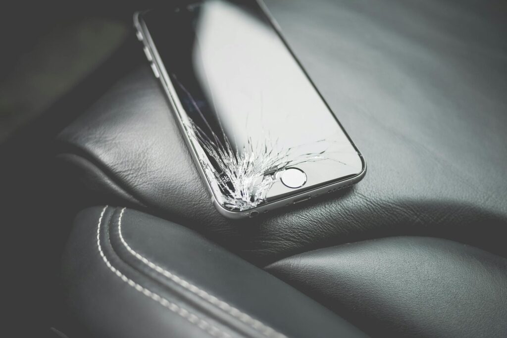 Telefon iphone z pękniętym w lewym dolnym rogu panelem wyświetlacza leżący na fotelu samochodowym