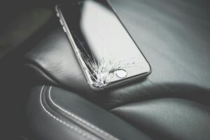 Telefon iphone z pękniętym w lewym dolnym rogu panelem wyświetlacza leżący na fotelu samochodowym