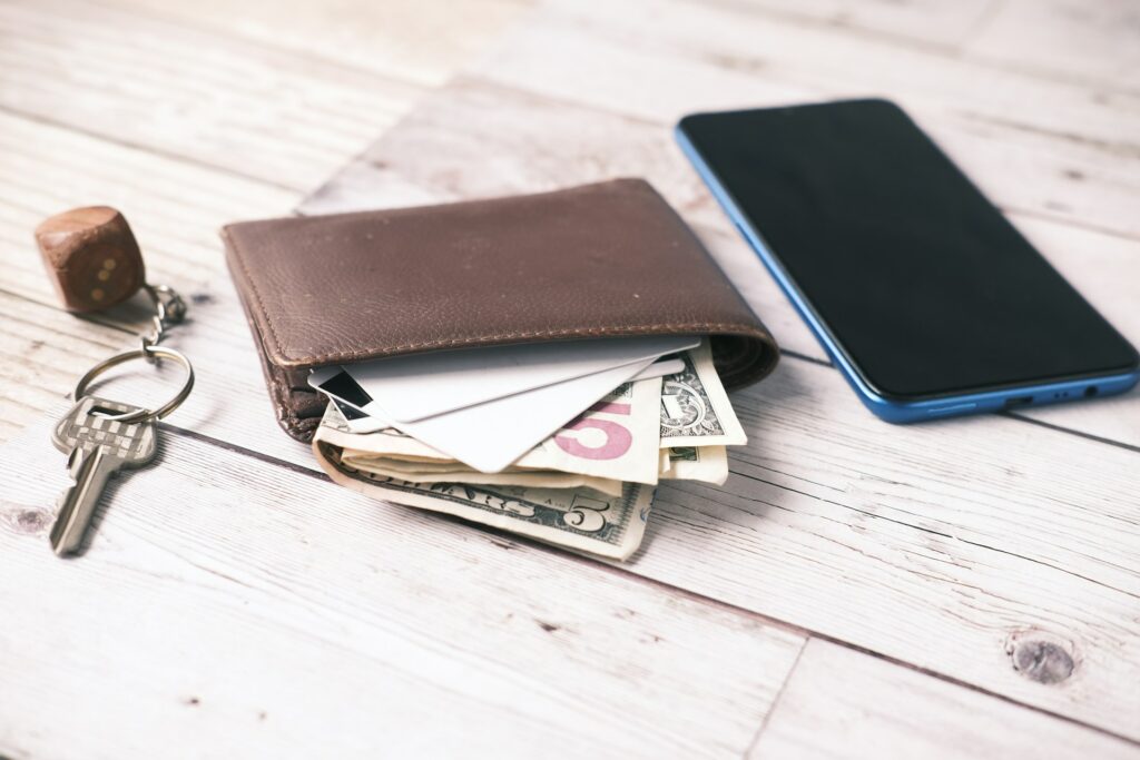 Portfel z gotówką i kartami obok smartfona na drewnianym stole — przygotowanie do zakupu używanego telefonu